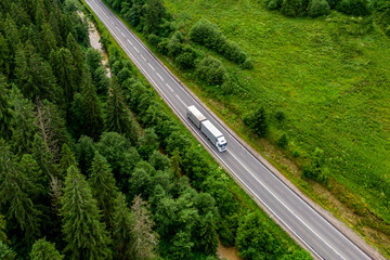 white truck driving on asphalt road on the highway. road through beautiful green forest. seen from the air. Aerial view landscape. drone photography. cargo delivery