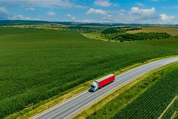 red truck driving on asphalt road on the highway. road through a beautiful green field on a background of blue clouds. seen from the air. Aerial view landscape. drone photography. cargo delivery