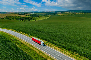 red truck driving on asphalt road along the green fields. seen from the air. Aerial view landscape. drone photography. cargo delivery . cargo delivery and transportation concept