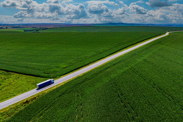 blue truck driving on asphalt road along the green fields. seen from the air. Aerial view...