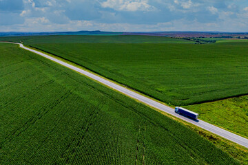 blue truck driving on asphalt road on the highway. road through a beautiful green field on a...