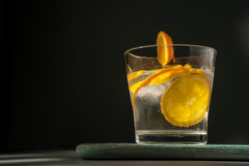 Glass of gin tonic with orange slice and ice. dark green background