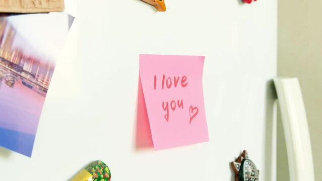 A woman's hand sticks a sticker with a note I Love You on the refrigerator door. 4K footage