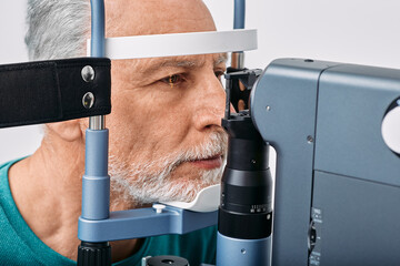 Senior man getting eye exam at ophthalmology clinic. Checking retina of male eye, close-up