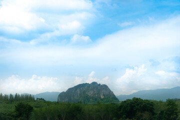 Obraz premium Landscape view of tall tree in front of agricultural areas. Mountain has a towering cliff in the middle. Under blue sky and white clounds. At Wang Chan, Rayong Thailand.