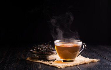 hot herbal teacup and dried tea leaves in a ceramic cup placed on a black wooden table on, dark...