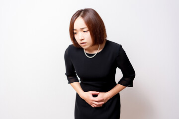 お腹を手で押さえている喪服を着ている女性