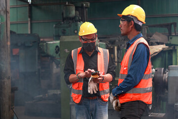 A team of Asian male engineers wearing safety helmets. Using smartphones in industrial factories, concepts, communication Production inspection, and metalworking projects in heavy industrial plants