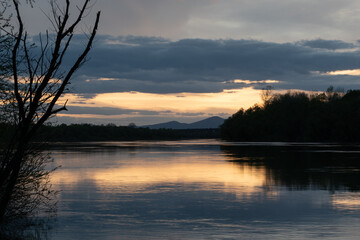 Landscape of river and mountain silhouette with cloudy sky, Sava river with forested shore and Motajica mountain during sunset with glow in clouds