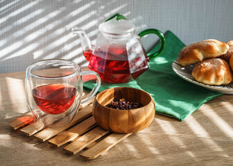 Hibiscus tea in a glass teapot and sweet buns on a plate on a wooden table with natural light