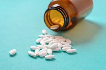 White oval medical pills pouring out of a medicine bottle on a blue background. Macro photo with copy space.