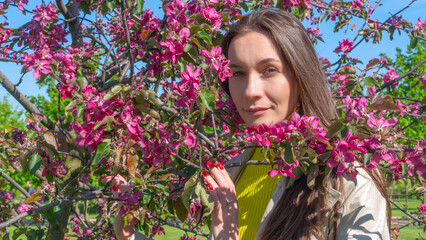 Portrait of beautiful young woman in paradise apple trees blooming park on a sunny day. Springtime. Red apple tree.