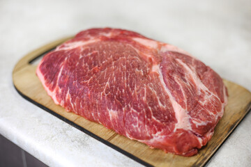 Big fresh piece of meat on wooden cutting board on light kitchen table