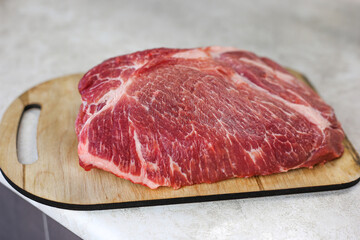 Big fresh piece of meat on wooden cutting board on light kitchen table