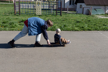 The older brother patiently and lovingly teaches the little boy his favorite hobby - to skate on a playground in the park in the fresh air.