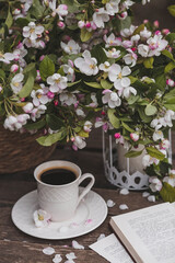 Obraz na płótnie Canvas A beautiful postcard. A white coffee cup with a saucer, a statuette, candles, a book and a vase with a bouquet of blooming apple trees. Beautiful still life. Spring time. The concept of 