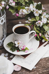 A beautiful postcard. A white coffee cup with a saucer, a statuette, candles, a book and a vase with a bouquet of blooming apple trees. Beautiful still life. Spring time. The concept of 