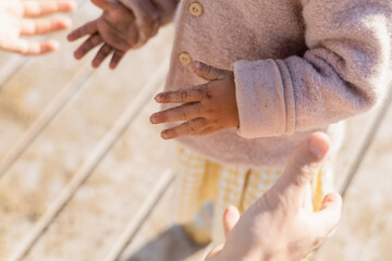 Cropped view of toddler girl with sand on hands standing near dad on beach.