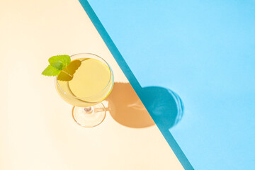 Summer scene with green cocktail on duo tone sandy and blue background. Pool party concept....