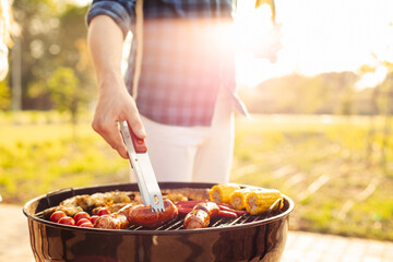 man prepares a barbecue for friends, happy friends make a barbecue outdoors at sunset, A man roasts meat on the grill - obrazy, fototapety, plakaty