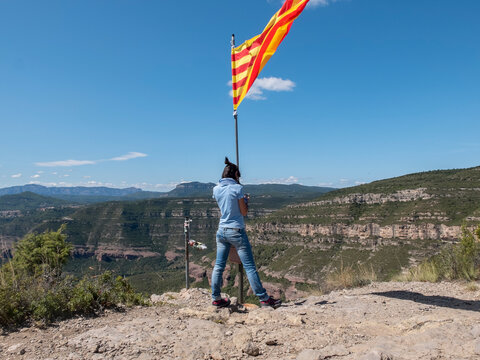 A lady holding a Catalonia flag on top mountain while using mobile