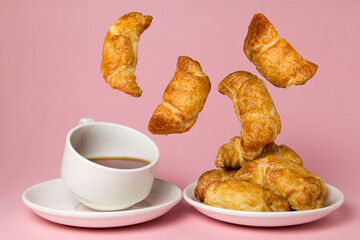 Cup of tea with croissants on a pink background. Tasty breakfast. Croissants fall into the plate