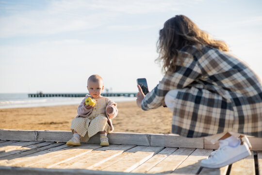 Blurred man taking photo of baby girl with apple on pier in Italy.