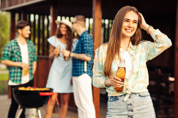 happy beautiful young woman with lemonade in the foreground, with a group of friends having a barbecue outdoors