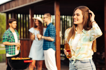 happy beautiful young woman with lemonade in the foreground, with a group of friends having a barbecue outdoors