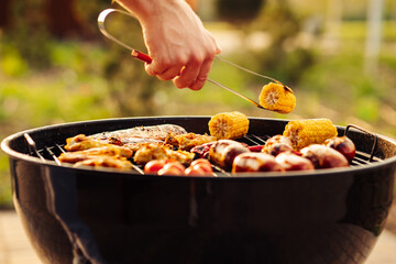 man prepares a barbecue for friends, happy friends make a barbecue outdoors at sunset, A man roasts meat on the grill