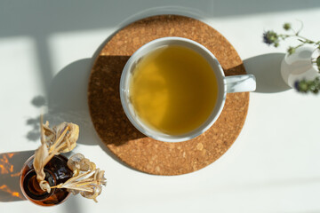 tea on a stand in a white mug with a vase of flowers on a white background in sunlight.