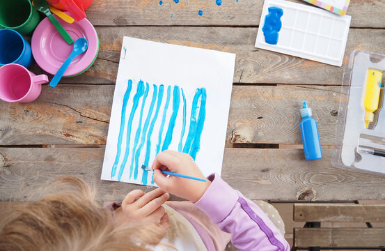 Ni&ntilde;a pintando l&iacute;neas azules - manos ni&ntilde;a y mesa de madera r&uacute;stica