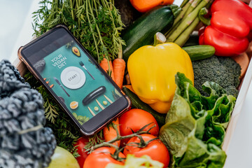 Go vegan. Top view wooden box with fresh vegetables and phone with active online mobile application with Vegan diet program. New Start of a healthy lifestyle, weight loss, food delivery concept. - obrazy, fototapety, plakaty