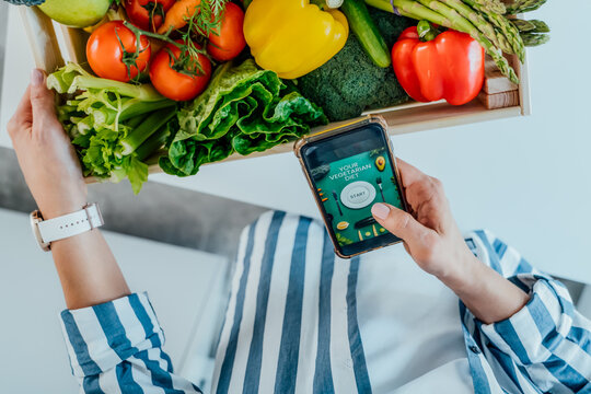 Top View Woman Holding Wooden Box With Fresh Vegetables And Phone With Active Online Mobile Application With Vegetarian Diet Program. New Start Of A Healthy Lifestyle, Weight Loss Concept.