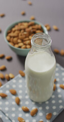Vertical image of a bowl of almonds and bottle of milk on lilac background