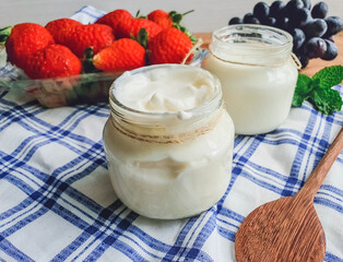 white natural yogurt in glass jar and on table  with fruits