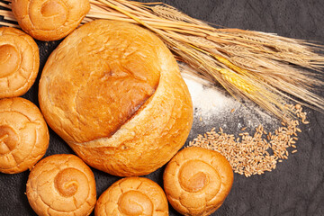 Culinary background with bread,sweet bun,wheat ears,grains on a black background, top view