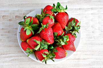 heap of fresh garden strawberries on plate on beige background, close-up