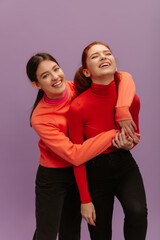 Obraz premium Pretty young caucasian girl hugging her sister standing in purple background. Teenagers in casual clothes laughing together. Lifestyle, different emotions, leisure concept. 
