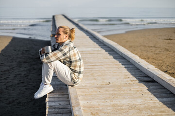 Young man in shirt holding metal cup on wooden pier in Treviso.