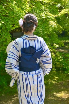 緑の新緑を背景に浴衣を着た若く美しい女性の後ろ姿