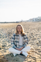 Young man with closed eyes meditating on beach in Italy.