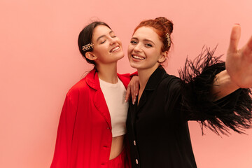 Modern young caucasian girls brunette, redhead take selfies on pink background. Models wear red and...