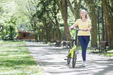 Retired woman resting in the park, gray-haired Persian woman walks with a bicycle on a summer day