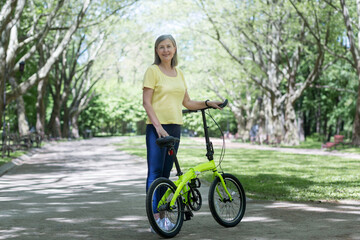 Naklejka premium Retired woman resting in the park, gray-haired Persian woman walks with a bicycle on a summer day