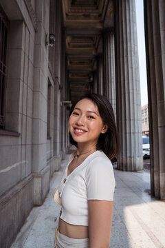 Content young Asian lady standing near building with columns in sunlight