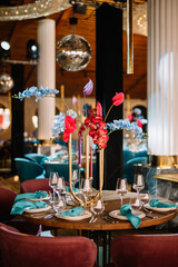 Wedding decorations. Festive table decorated with compositions of colored flowers. On the tables are plates, glasses, candles and cutlery