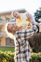 Positive man looking at camera while holding baby daughter on urban street in Treviso.