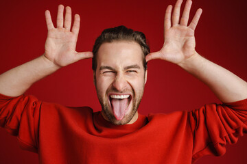 Young bristle man wearing sweater gesturing while showing his tongue - obrazy, fototapety, plakaty