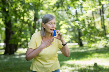 Senior retired woman with asthma breathing in an inhaler in a summer park